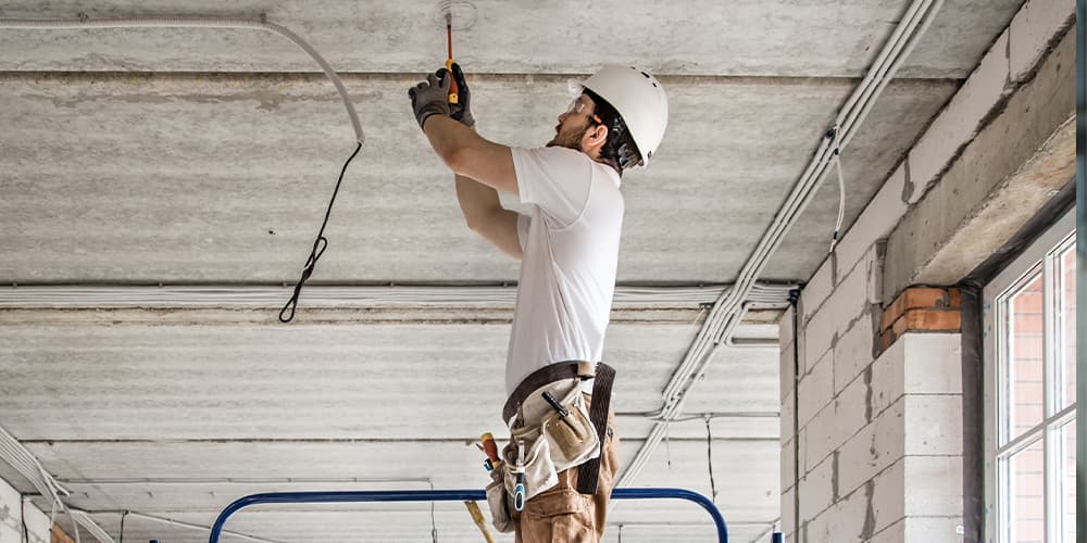 Electrician working on ceiling wiring inside a building under construction