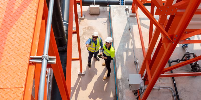 Two utilities workers standing on a concrete platform discussing plans at a worksite